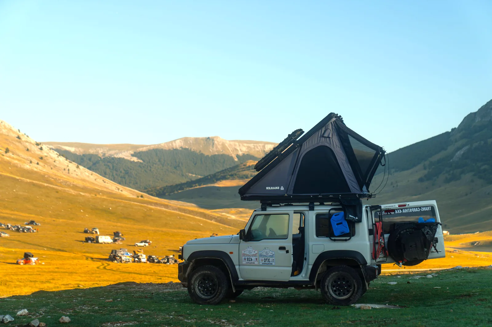 Fuoristrada con tenda da tetto SNAILER aperta in un campeggio di montagna
