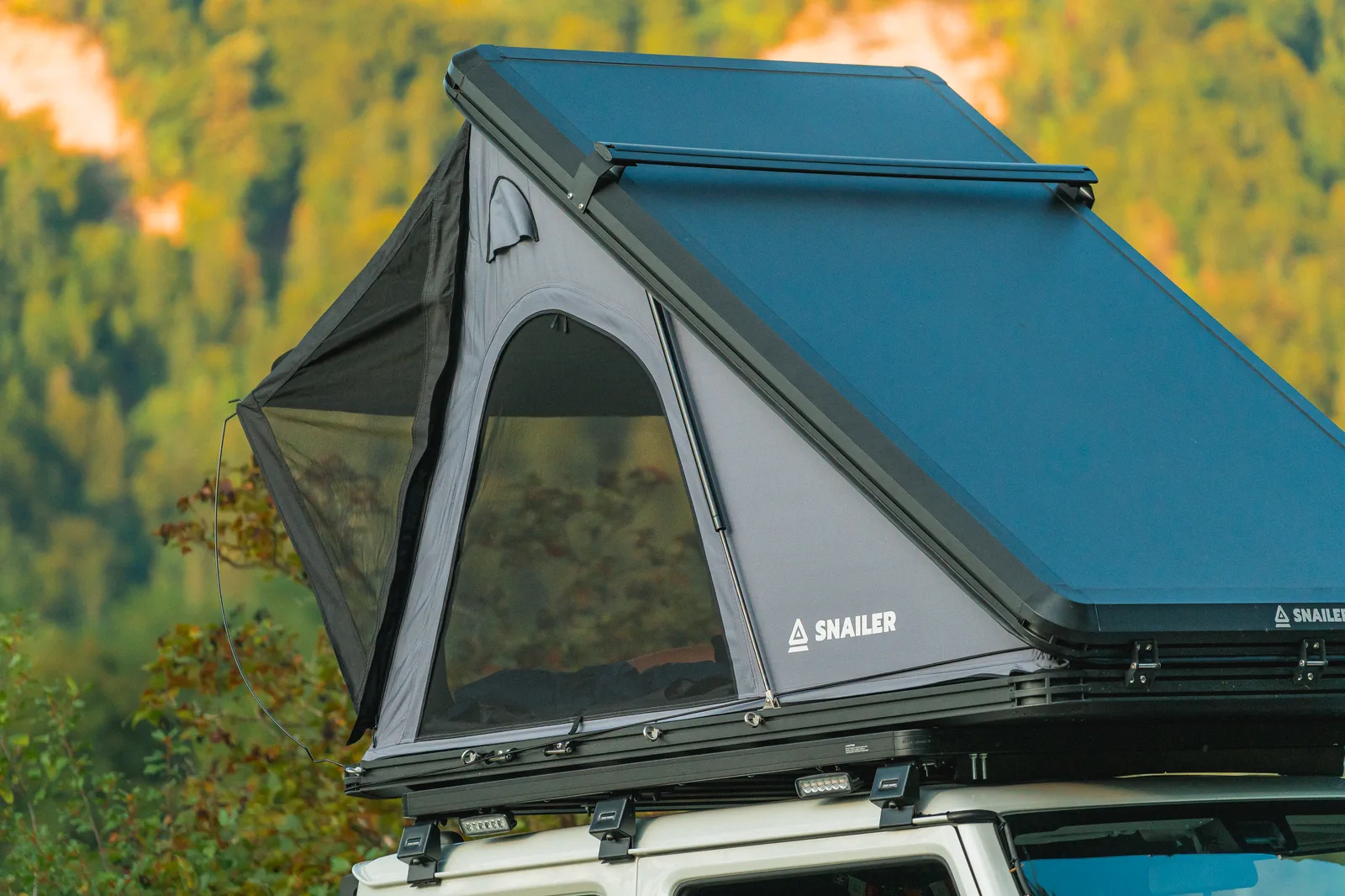 Tenda da tetto rigida SNAILER aperta accanto a un bosco